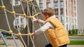 Little active boy climbing up the rope spider web on outdoor children playground on the sunny autumn day Royalty Free Stock Photo