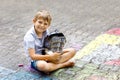 Little active kid boy drawing knight castle and fortress with colorful chalks on asphalt. Happy child with big helmet