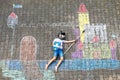 Little active kid boy drawing knight castle and fortress with colorful chalks on asphalt. Happy child in helmet and with