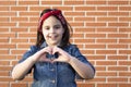 Little activist girl forming heart with her hands isolated on brick wall. Love and feminist future