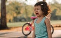 Little adorable angry caucasian curly hair girl standing outdoor in garden in summer holiday at evening, crying with sadness, Royalty Free Stock Photo