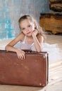 Little adorable ballerina in white tutu with old vintage suitcase in a beautiful studio. Travel and voyage. Concept of growing up