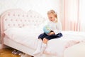 Little adorable blonde girl in school uniform and white golfs siting on a ber in her bedroom with globe in her hands Royalty Free Stock Photo