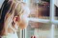 Little adorable blonde toddler girl looking through a window with rain drops on it. Close up portrait Royalty Free Stock Photo