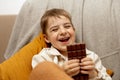 Little adorable boy sitting on the couch at home and eating chocolate bar. Child and sweets, sugar confectionery. Kid Royalty Free Stock Photo