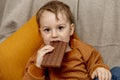 Little adorable boy sitting on the couch at home and eating chocolate bar. Child and sweets, sugar confectionery. Kid Royalty Free Stock Photo