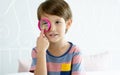 Little adorable Caucasian boy wearing casual cloth, standing, holding and playing magnifying glass as toy to investigate,