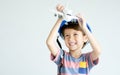 Little adorable Caucasian boy wearing hard hat, standing on white background, holding and playing airplane toy, smiling with