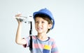 Little adorable Caucasian boy wearing hard hat, standing on white background, holding and playing airplane toy, smiling with