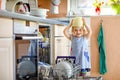 Little adorable child helping to unload dishwasher. Funny happy toddler girl standing in the kitchen, holding dishes and