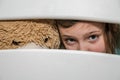 Little adorable girl child with a teddy bear looks through a crack in a hole in a wooden fence Royalty Free Stock Photo