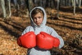 Little adorable girl child in a tracksuit, with a hood on his head, in red boxing gloves, boxing on the street in the autumn fores Royalty Free Stock Photo