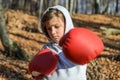 Little adorable girl child in a tracksuit, with a hood on his head, in red boxing gloves, boxing on the street in the autumn fores Royalty Free Stock Photo