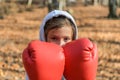 Little adorable girl child in a tracksuit, with a hood on his head, in red boxing gloves, boxing on the street in the autumn fores Royalty Free Stock Photo