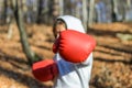 Little adorable girl child in a tracksuit, with a hood on his head, in red boxing gloves, boxing on the street in the autumn fores Royalty Free Stock Photo