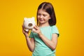 Little adorable girl holding money box in shape of pig near ear looking happy Royalty Free Stock Photo