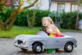 Little adorable toddler girl driving big vintage toy car and having fun with playing outdoors. Crying sad upset child on Royalty Free Stock Photo