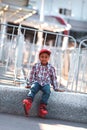 Little african american boy in casual wear and roller skates sitting alone on stone parapet and waiting his turn. Royalty Free Stock Photo