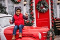 Little african american boy sitting on the hood of Christmas vintage car. Child fooling around Royalty Free Stock Photo