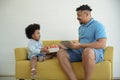 A Little African American boy surprise give his father a gift box at home
