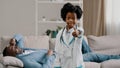 Little african american daughter playing with dad father patient lying on couch kid girl pretending to be doctor looking Royalty Free Stock Photo