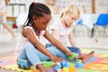 Little african american girl and classmate playing with colourful educational toy blocks on the floor at preschool or