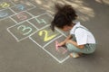 Little African American girl drawing hopscotch with chalk on asphalt outdoors. Happy childhood Royalty Free Stock Photo