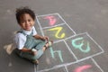 Little African American girl drawing hopscotch with chalk on asphalt outdoors. Happy childhood Royalty Free Stock Photo