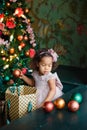 A little African-American girl in a pink dress with Christmas balls near the Christmas tree. the child decorates