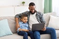 Little African Boy And Dad Watching Cartoons On Laptop Indoor