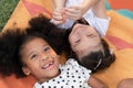 Little African and Caucasian kids girls smiling laughing and lying together on colorful mat on green grass Royalty Free Stock Photo