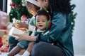 Little African child boy is sitting smiling in arms of Asian young mother with earmuffs enjoy celebrating Christmas at home Royalty Free Stock Photo