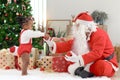 Little African cute girl giving red ornament balls to Santa Claus for decorating beautiful Christmas tree. Happy baby kid and Royalty Free Stock Photo