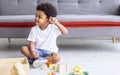 Little african cute playful boy sitting on the floor and playing toys alone in living room at home or apartment in holidays. Royalty Free Stock Photo
