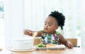 Little African hungry toddler girl filling plate with spaghetti from pot, eating spaghetti and vegetables with fork in kitchen at Royalty Free Stock Photo