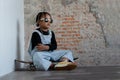 Little African kid boy with dreadlock hairstyle wear cool gold sunglasses, necklace chain, jeans bib and sneaker cross his arms
