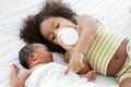 Little African older sister sucking milk from bottle and take good care of her newborn baby brother lying on bed at home Royalty Free Stock Photo