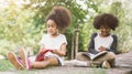 Little Afro child girl reading book between green spikes meadow garden with friend