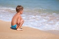 Little alone boy sitting on the beach near water Royalty Free Stock Photo