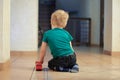 Little alone caucasian baby boy with fair hair sits on the floor, back to the viewer, with red bus toy. Loneliness concept. Royalty Free Stock Photo