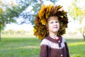 Little amusing girl in a wreath from autumn leaves