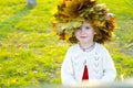 Little amusing girl in a wreath from autumn leaves