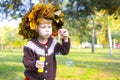 Little amusing girl in a wreath from autumn leaves