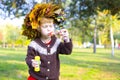 Little amusing girl in a wreath from autumn leaves