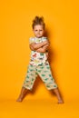 Angry blond boy preschooler in pajamas with dinosaurs having fun has joy in the studio over yellow background.