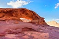 Little arc or small rock window formation in Wadi Rum desert, bright sun shines on red dust and rocks, blue sky above Royalty Free Stock Photo