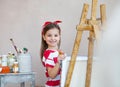 Little artist girl holding a paintbrush and looking over a canvas