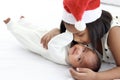 Little Asian African newborn infant baby girl lying on white bed with sister wearing red Christmas Santa hat while hugging and Royalty Free Stock Photo