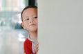 Little Asian baby boy hide behind a corner room. Small children playing peekaboo game indoor