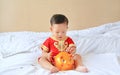 Little Asian baby boy in traditional Chinese dress putting some coins into a piggy bank sitting on bed at home. Kid saving money Royalty Free Stock Photo